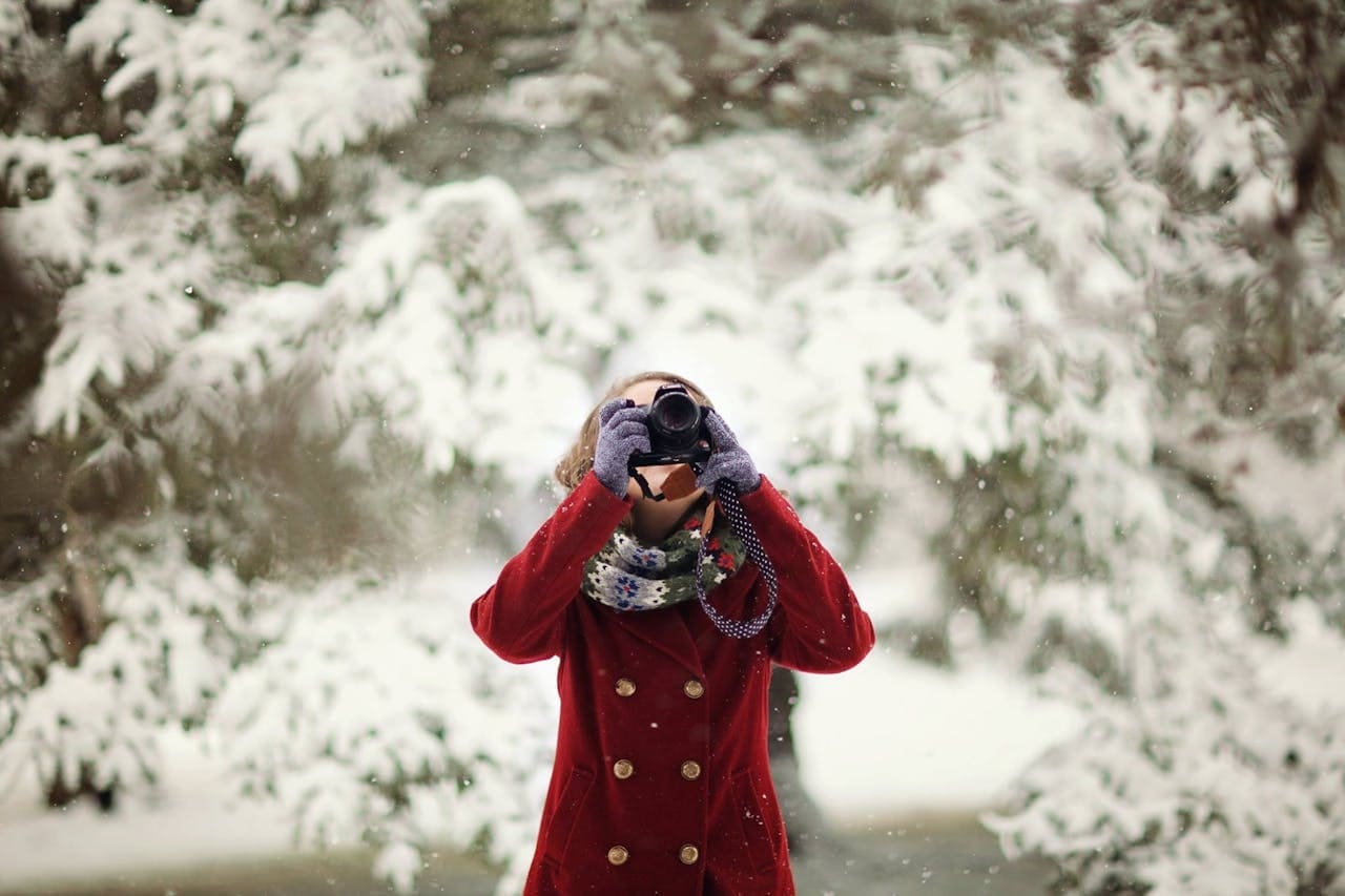 The Ultimate Winter Escapes for the Elite Traveller a woman taking pictures surrounded by snow